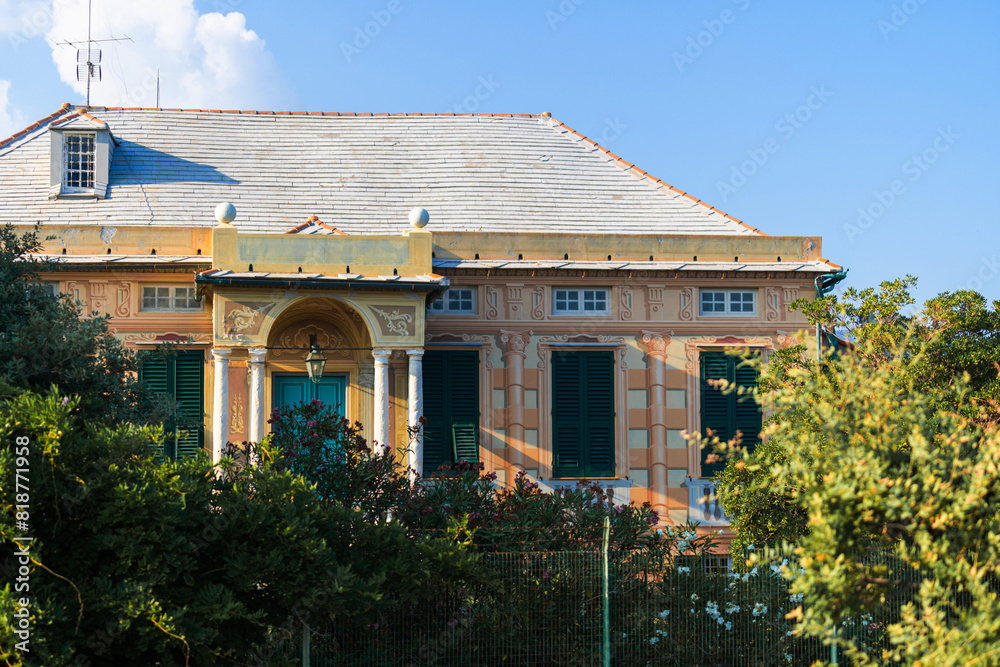 Fototapeta premium charming vintage villa with green shutters and ornate columns, surrounded by lush greenery under a clear blue sky