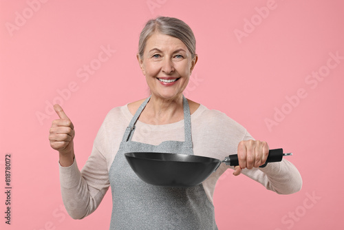 Happy housewife with frying pan showing thumbs up on pink background