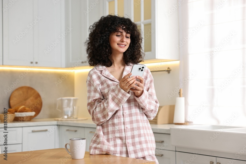 Beautiful young woman in stylish pyjama with smartphone in kitchen Beautiful young woman in stylish pyjama with smartphone in kitchen