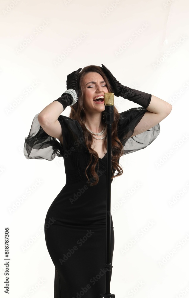 Beautiful young woman in stylish black dress with microphone singing on light background Beautiful young woman in stylish black dress with microphone singing on light background