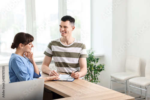 Smiling medical assistant working with patient at hospital reception. Space for text