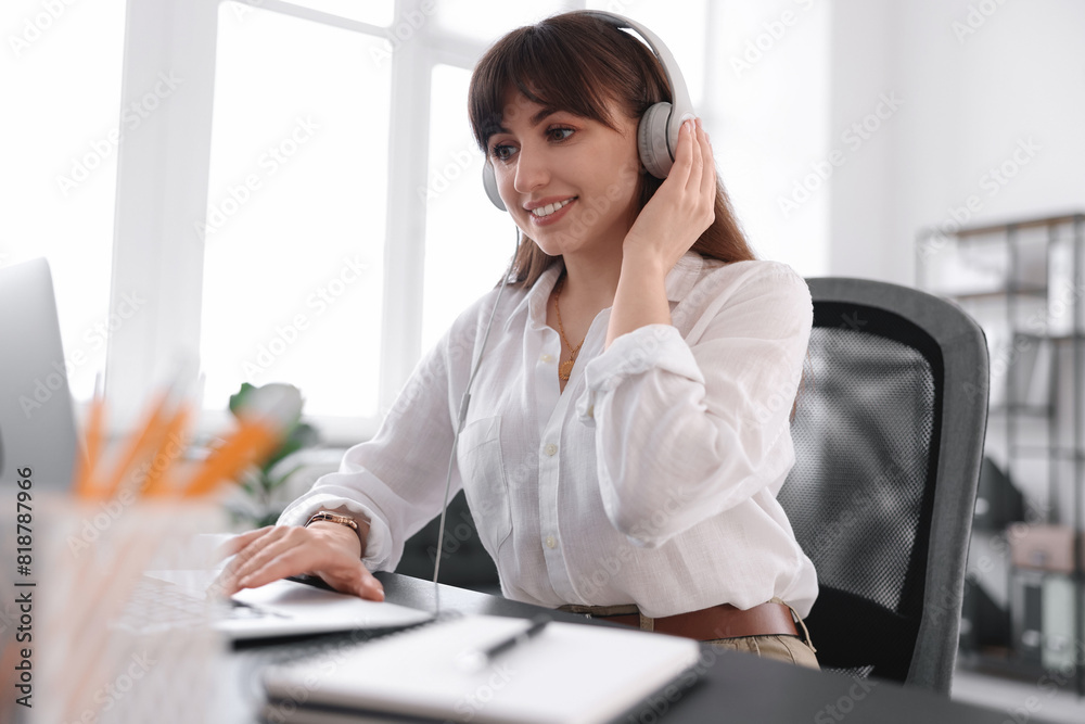 Woman in headphones watching webinar at table in office Woman in headphones watching webinar at table in office