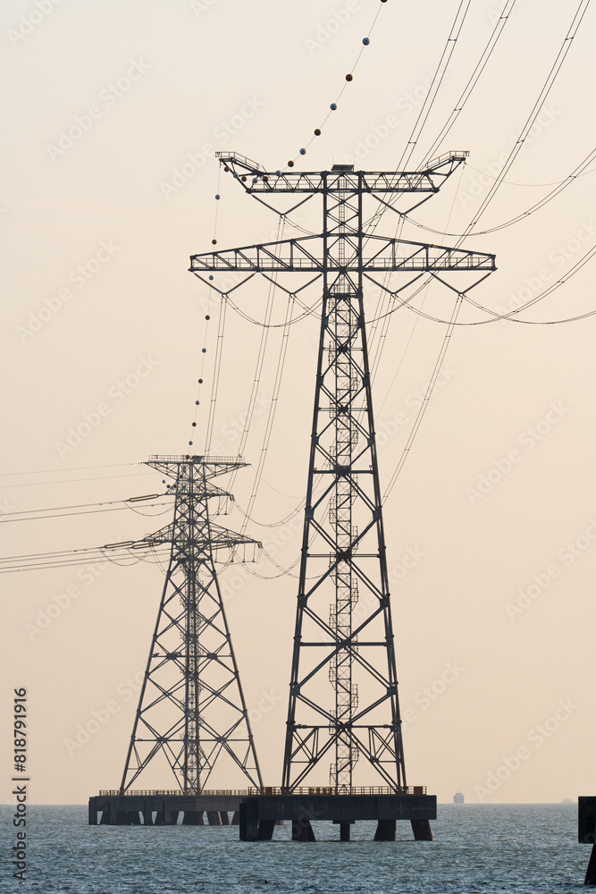 High voltage transmission towers over sea water in sunset