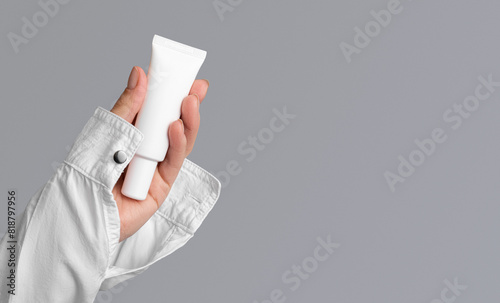 Cosmetic tube in hands in a white shirt on a gray background with copy space