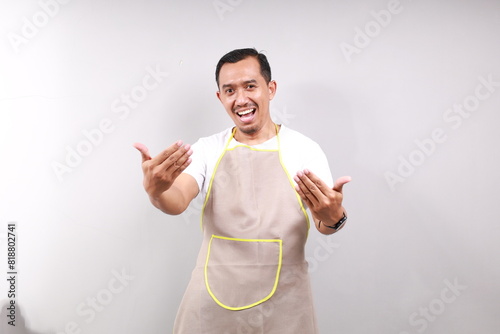 Asian man wearing an apron isolated on gray background inviting to come with hand. Happy that you came photo