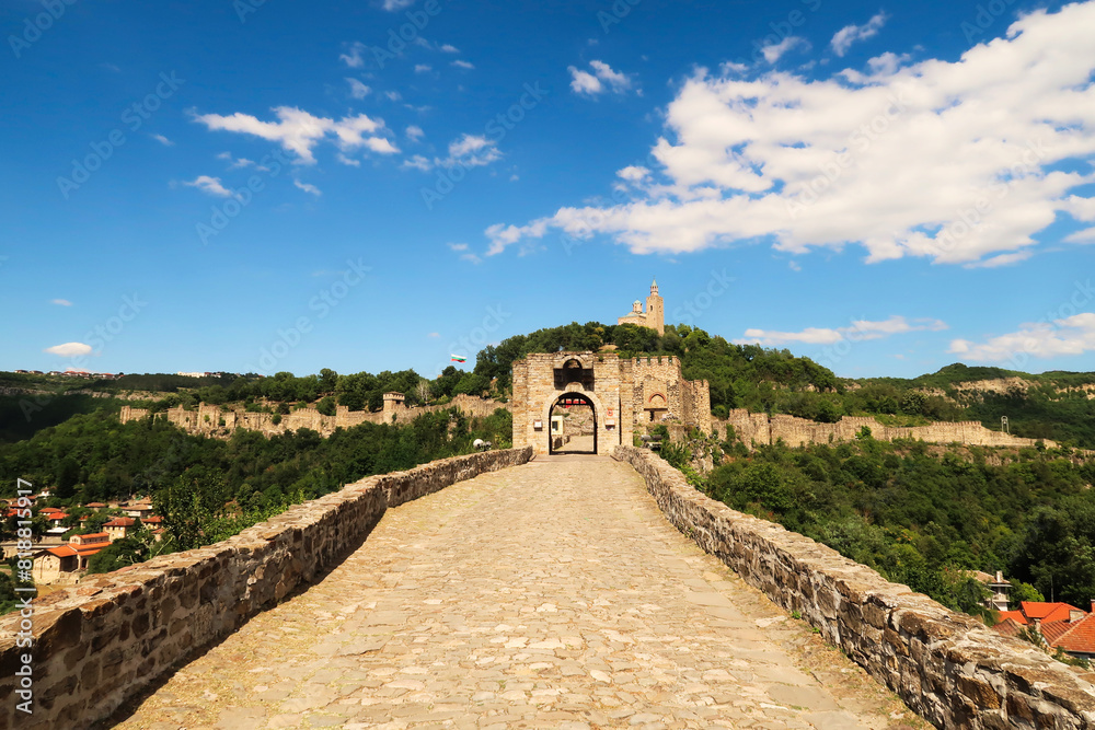 Fototapeta premium Cobble stone street to the entrance gate of the Tsarevets Fortress, its walls and the Patriarchal Cathedral, Church of the Holy Ascension of the Lord seen in the background, Veliko Tarnovo, Bulgaria