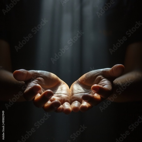 A pair of hands stretched towards the light, symbolizing hope and healing in an emotional setting. Black dark background. Soft light shines down from above, the light focuses on the fingers