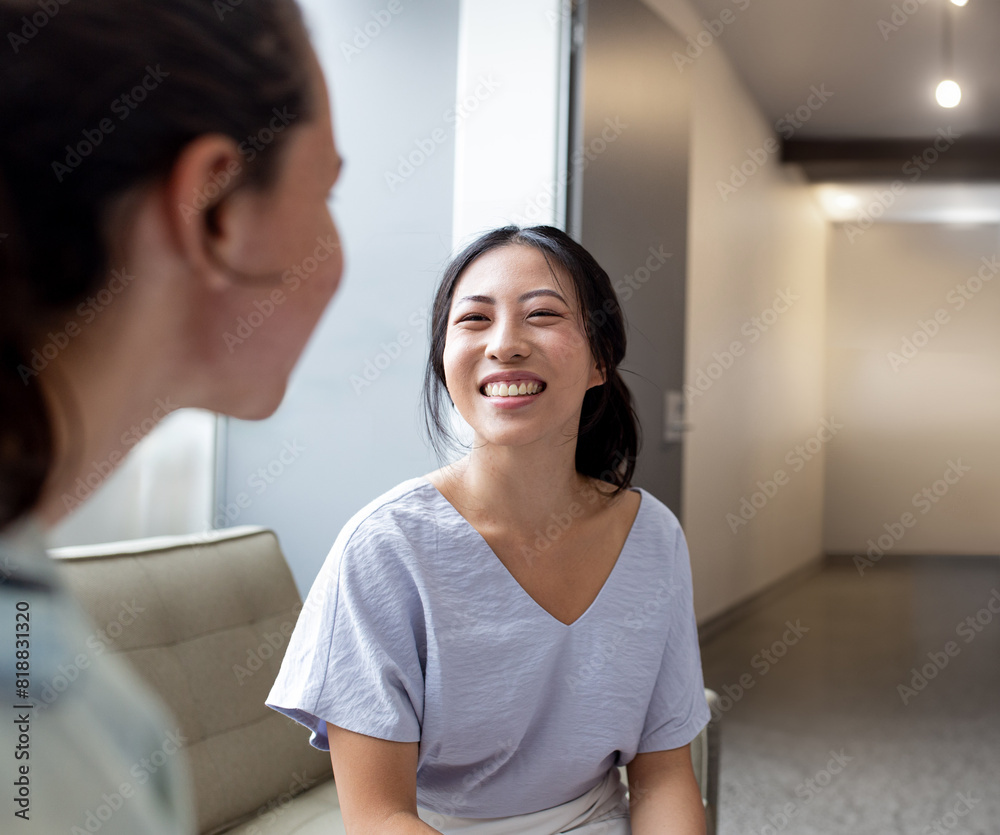 Happy Asian woman sitting on a sofa talking with a colleague smiling Happy Asian woman sitting on a sofa talking with a colleague smiling
