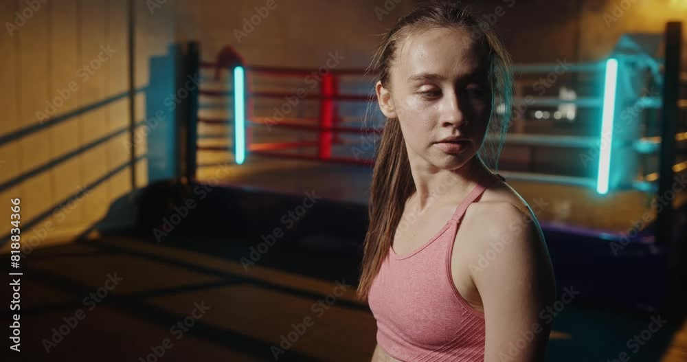 Portrait of a young female boxer in a gym with an illuminated boxing ring in the background, showcasing determination, fitness, and an active lifestyle in a modern workout environment Portrait of a young female boxer in a gym with an illuminated boxing ring in the background, showcasing determination, fitness, and an active lifestyle in a modern workout environment