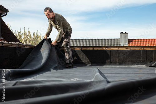 A craftsman rolls out a thick rubber tarpaulin on a flat roof
