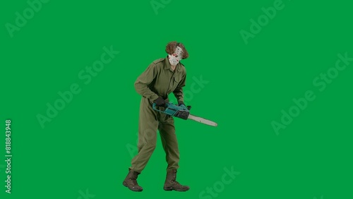 A maniac in a hockey mask and overalls with a chainsaw in his hands walks and looks around. Unrecognizable man in scary Jason Voorhees look on green screen chromakey. Halloween, horror.