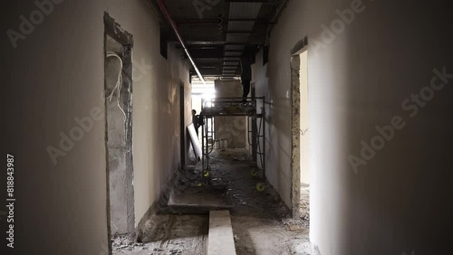 Worker on scaffold at construction inside unfinished building. Hallway with cables, concrete raw walls. Works in process 
