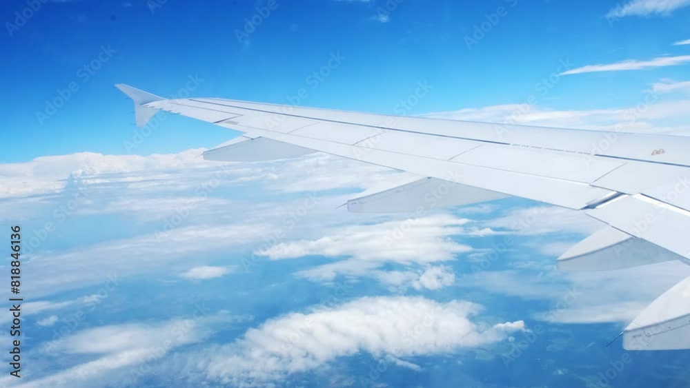 View of an airplane wing from a porthole against a blue sky background. A passenger plane flies above the clouds in the morning light. The concept of traveling by air. Fear of heights, aerophobia. 4K