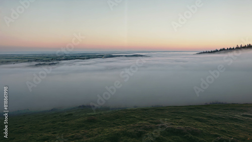 landscape with cloud inversion  a grassy hill in the foreground and distant hills emerging above a dense fluffy layer of clouds