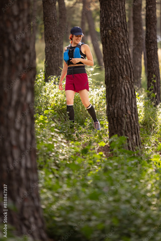 A woman is walking through a forest wearing a blue and black backpack A woman is walking through a forest wearing a blue and black backpack