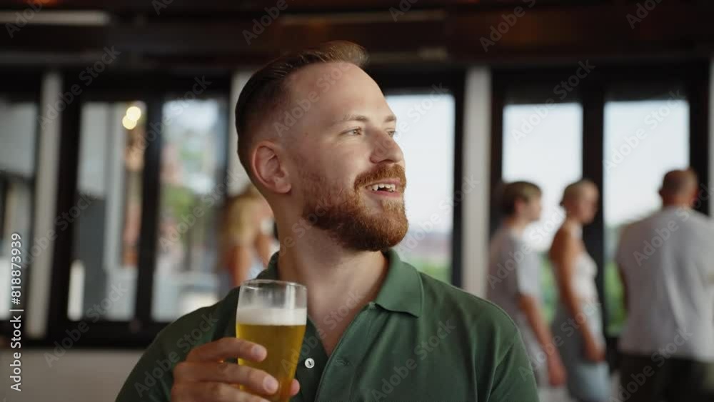 Bearded young man drinking beer with foam in the restaurant bar full of people. Enjoying drinks in cafe. Medium shot with natural light Bearded young man drinking beer with foam in the restaurant bar full of people. Enjoying drinks in cafe. Medium shot with natural light