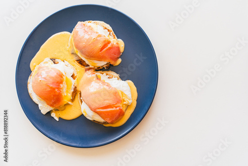 Toast with eggs benedict, salmon and hollandaise sauce on a blue plate on a white background. Space for text