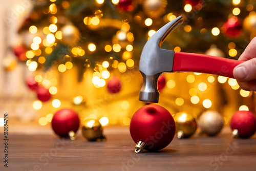 Hammer in male hand above the red christmas ball, going to break it, close up. Christmas decoration, lack of christmas mood, end of winter holidays concept