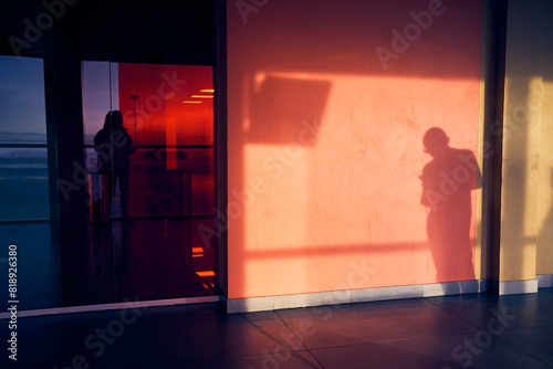 The man looks at the smartphone. The red shade of a part of the wall with space to copy. The shadow of a young passerby on a stone wall. Sunlight creates a drawing of a person. High quality photo