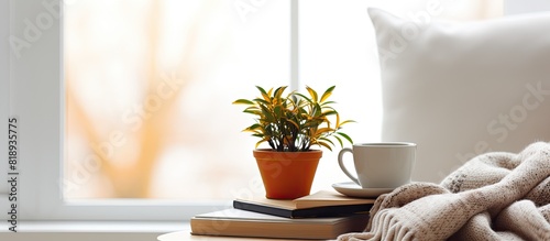 The cozy interior decor of a home includes a cup of coffee a stack of books potted plants on a wicker stand and pillows and plaid on a white table This concept is aligned with staying at home during photo