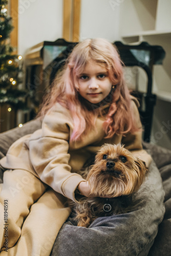 Beautiful little girl with a Yorkshire terrier sitting on a gray ottoman.