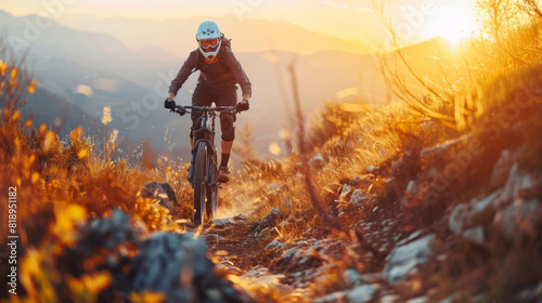 A mountain biker in full gear speeds down a rocky mountain path during a vibrant sunset. © khonkangrua