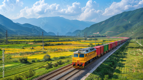 Bright yellow cargo train moving swiftly through lush green fields with mountains in the background under a clear sky.
