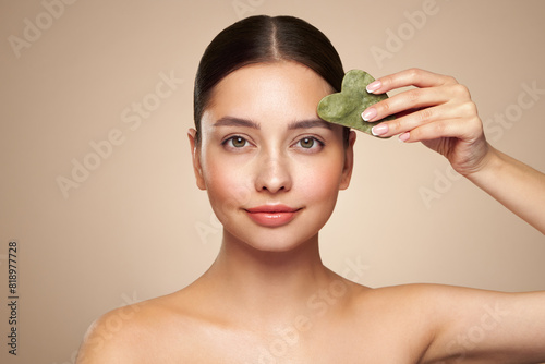 Beauty young woman doing skin care routine, scrapping, massage facial skin with jade gua sha scrapper, Facial treatment for anti aging and cosmetic cleaning photo