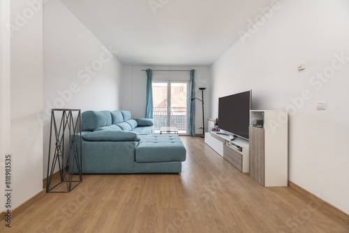 Living room with a large sofa upholstered in blue fabric and a balcony with matching curtains