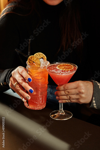 Women clinking glasses with colorful cocktails in dimly lit bar