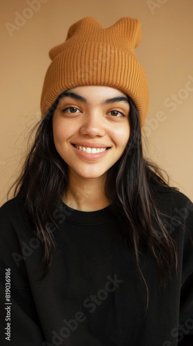 young woman with dark hair, wearing cute black sweatshirt and golden brown beanie hat smiling © Worrapol