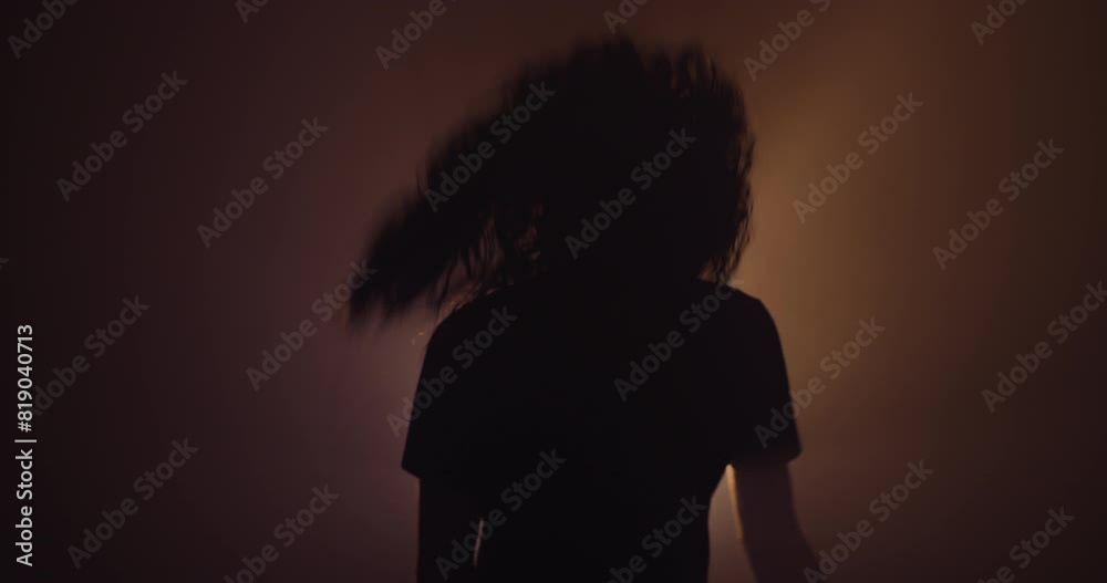 Silhouette of a person with long hair head banging 