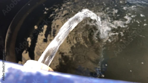 Top view of a blue water tank being refilled with clear drinking water from a pipe. Lack of water