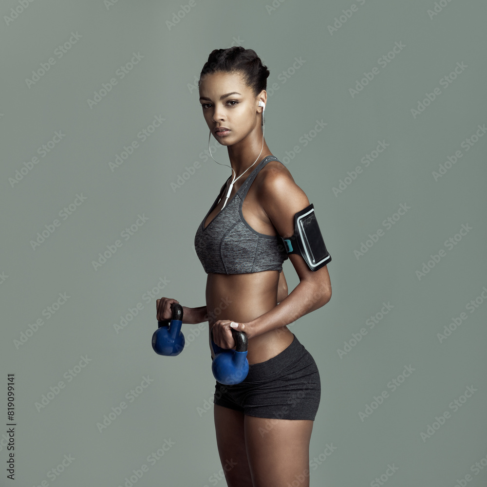 Studio portrait, woman and kettlebell for workout with earphones, streaming kpop music and arm exercise. Weights, listening to sound and athlete girl by gray background for sports training and audio