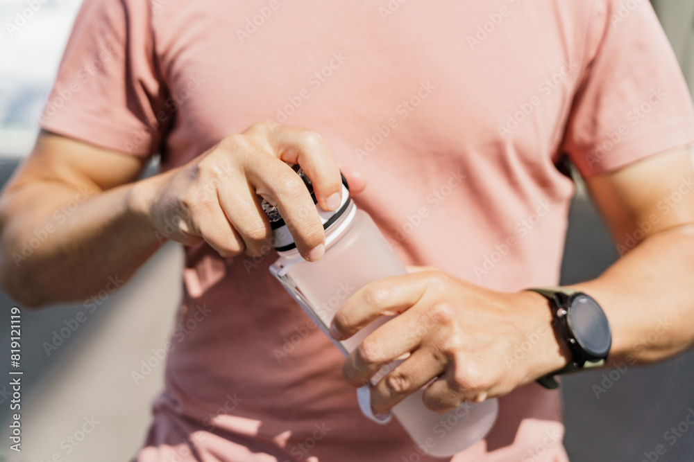 A close-up of a man opening a water bottle, highlighting hydration during an outdoor workout.