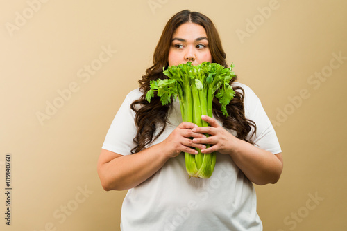 Latin plus-size woman playfully posing with a bunch of fresh celery in a studio setting