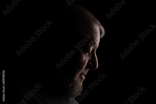 Low key dark dramatic profile portrait closeup silhouette photo of 82 year old octogenarian Caucasian man