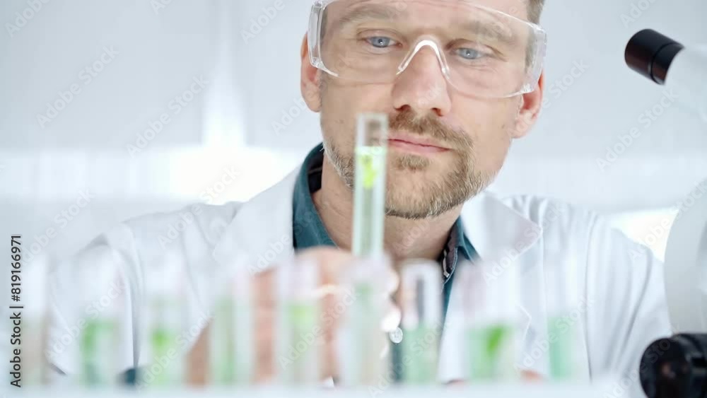 Man researcher with safety glasses is examining lab tube with a green fluid in a modern laboratory, close-up. Science, microbiology and medicine Man researcher with safety glasses is examining lab tube with a green fluid in a modern laboratory, close-up. Science, microbiology and medicine