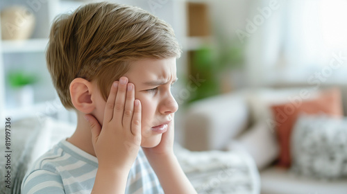 Sad little boy holding his head suffering from migraine. Headache in children. home interior with copy space