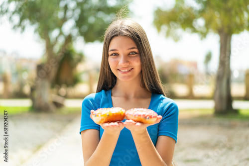 Teenager girl at outdoors holding donuts with happy expression