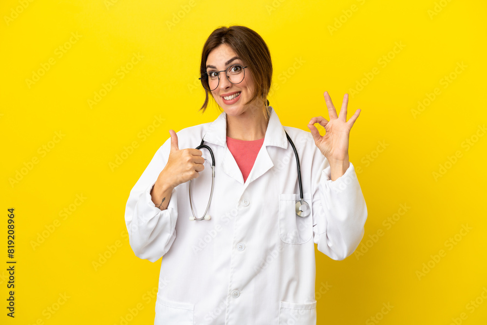 Doctor woman isolated on yellow background showing ok sign and thumb up gesture