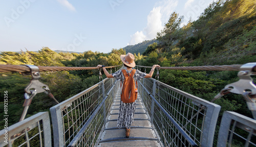 girl in a hat walks along a suspension bridge. Autumn season outdoors, portrait of a woman walking on a suspension bridge over a river.