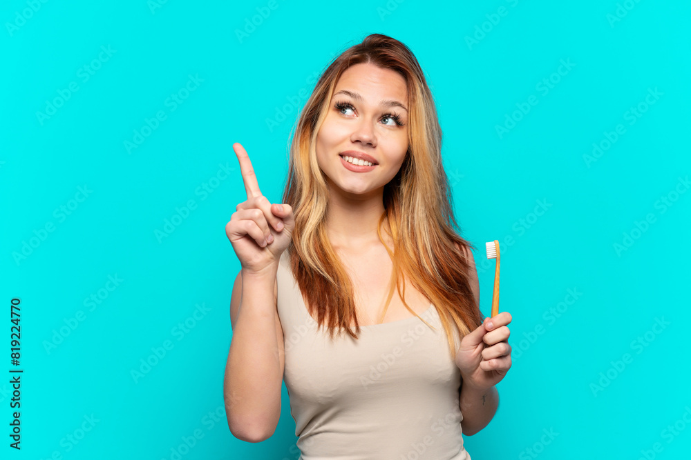 Teenager girl brushing teeth over isolated blue background pointing up a great idea Teenager girl brushing teeth over isolated blue background pointing up a great idea