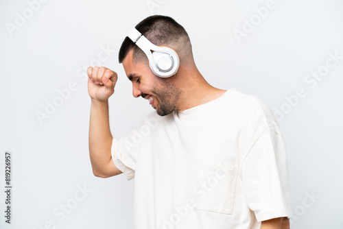 Young caucasian man isolated on white background listening music and dancing