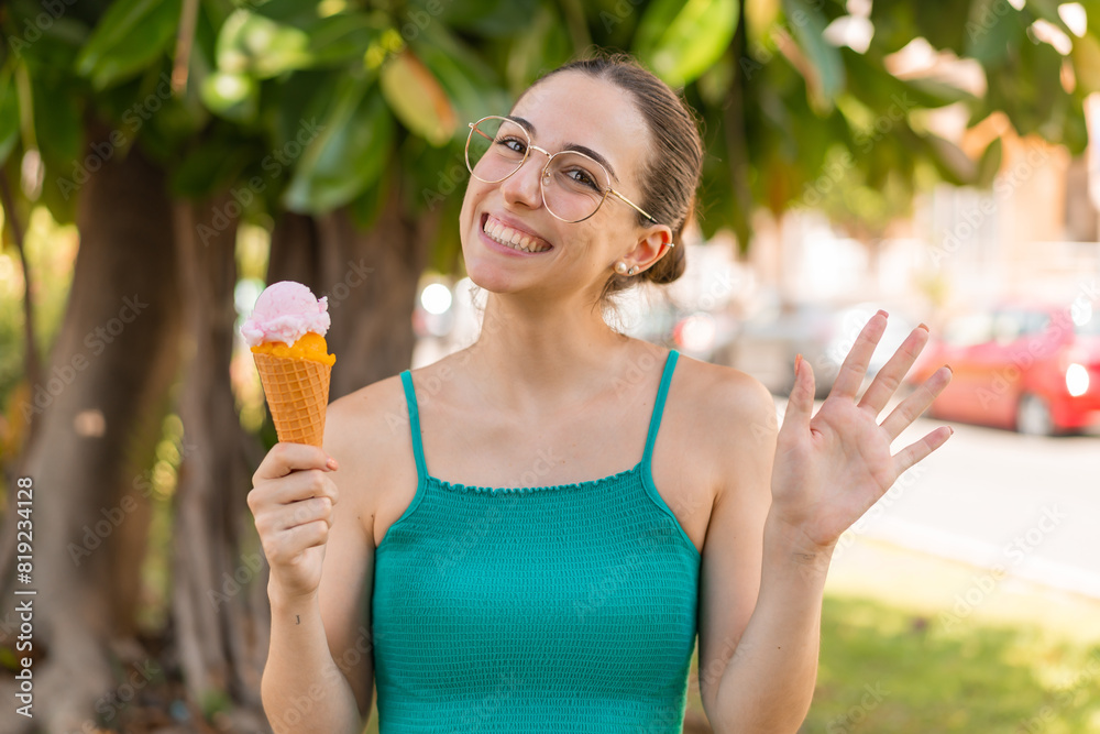 Young pretty woman with a cornet ice cream at outdoors saluting with hand with happy expression Young pretty woman with a cornet ice cream at outdoors saluting with hand with happy expression