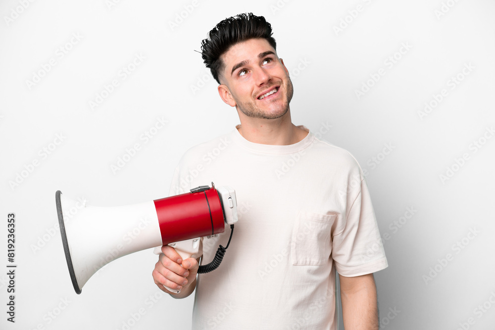 Young caucasian man isolated on white background holding a megaphone and looking up while smiling Young caucasian man isolated on white background holding a megaphone and looking up while smiling
