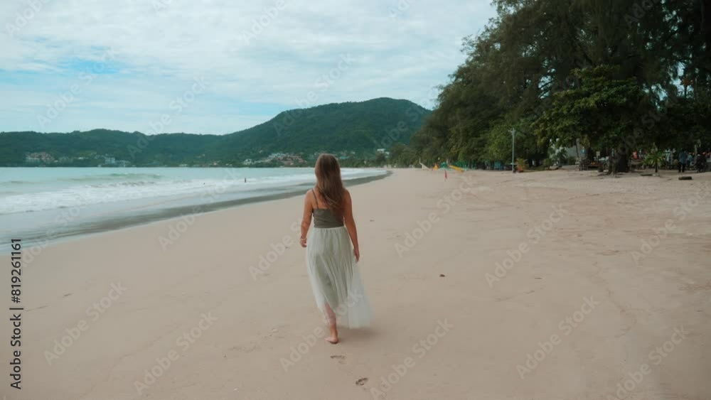 Woman walks alone on sandy beach during daytime, enjoying serene natural scenery with trees in background. Peaceful and relaxing outdoor activity in tropical destination. Travel and leisure. Woman walks alone on sandy beach during daytime, enjoying serene natural scenery with trees in background. Peaceful and relaxing outdoor activity in tropical destination. Travel and leisure.