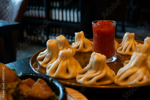 A plate of khinkali Georgian dumplings with adjika sauce in a restaurant, bottles of wine in the background photo