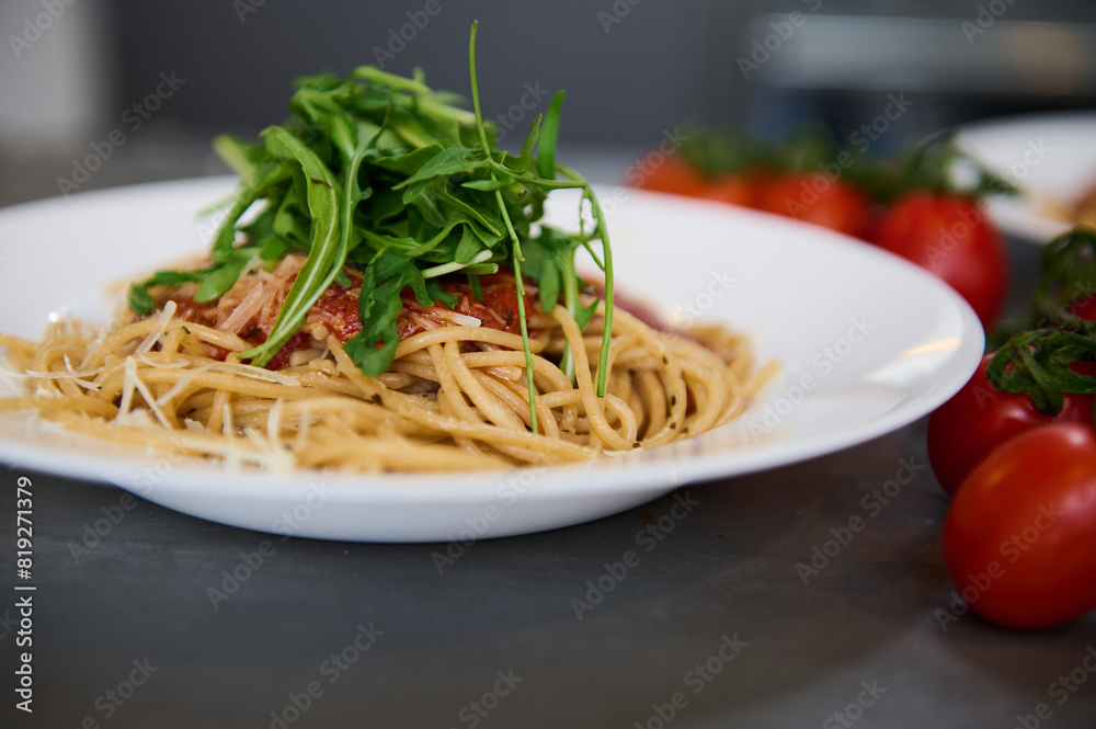 Italian pasta. Fresh homemade spaghetti capellini pasta with tomato sauce and garnished with arugula green leaves on the kitchen table near a branch of organic tomato cherry Italian pasta. Fresh homemade spaghetti capellini pasta with tomato sauce and garnished with arugula green leaves on the kitchen table near a branch of organic tomato cherry