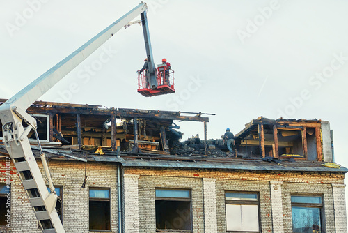 Фотография Unrecognizable workers in crane cradle dismantling charred roof after fire, aftermath of an emergency